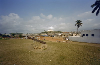 EU: Stadsgezicht met fort op de achtergrond en kanon van Elmina Castle op de voorgrond, Elmina, 2000