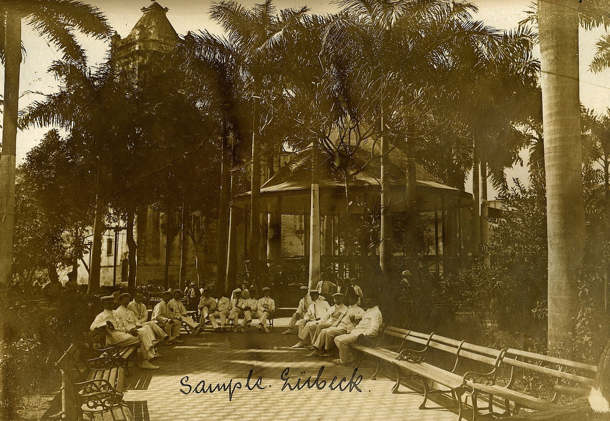 EU: Panama-Stadt. Herren in weißen Marineanzügen auf Parkbänken in einem Palmengarten vor dem Musikpavillon, im Hintergrund eine Kirche (1915), Panama City, Panama, 1915