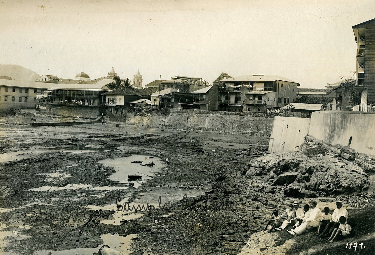 EU: Panama-Stadt. Drei Touristen der Hapag mit einheimischen Kindern auf Felsen vor ausgetrocknetem Hafenbecken oder Bucht sitzend (1915), Panama City, Panama, 1915