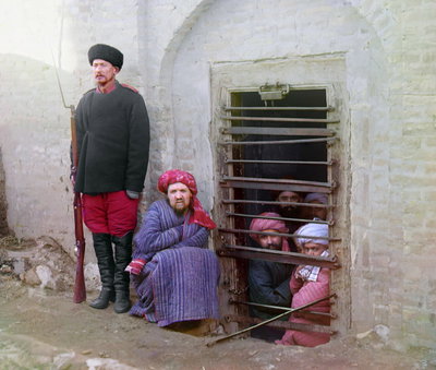 Zindan (traditional Central Asian prison), with inmates looking out through the bars and a guard with Russian rifle,…, Bukhara, 1905