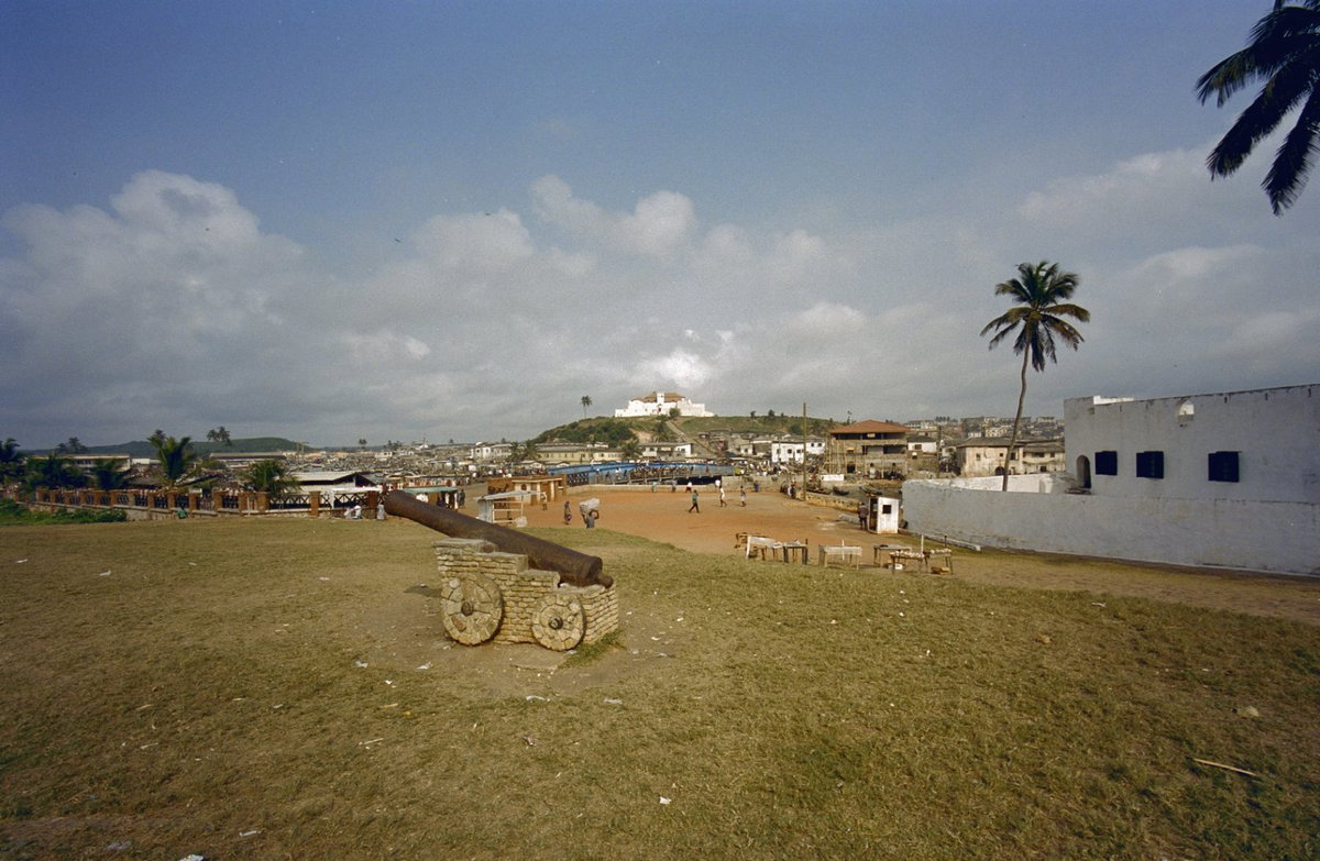 EU: Stadsgezicht met fort op de achtergrond en kanon van Elmina Castle op de voorgrond, Ghana reis Loek Tangel (2000), Elmina, Ghana, 2000